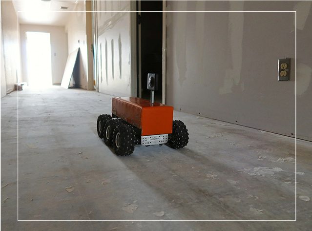 A red robot is on the floor of an empty room.